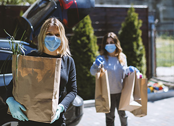 Two women with masks and gloves delivering groceries